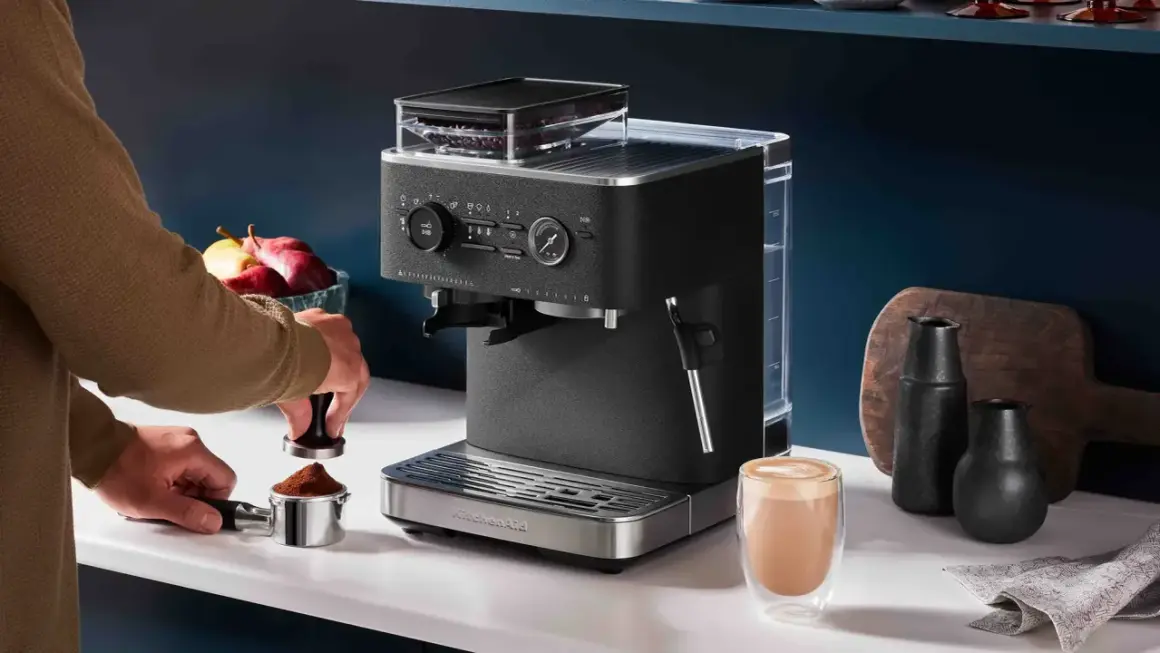 Un uomo prepara il miglior caffè con una macchina KitchenAid. Un bicchiere di cappuccino fumante attende sul bancone.