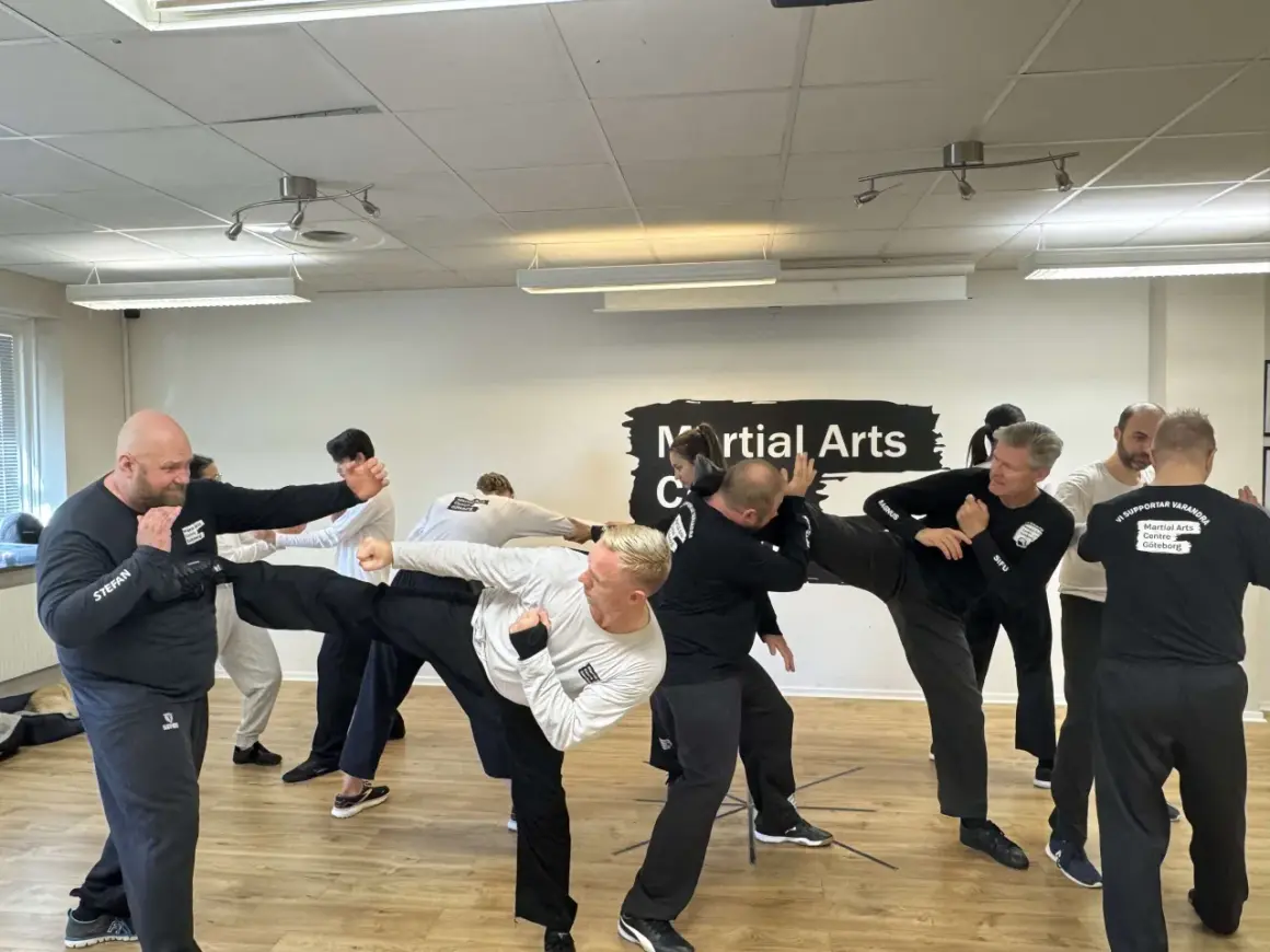 Män tränar wing chun i en lokal. En man utför en hög spark medan andra övar försvar.