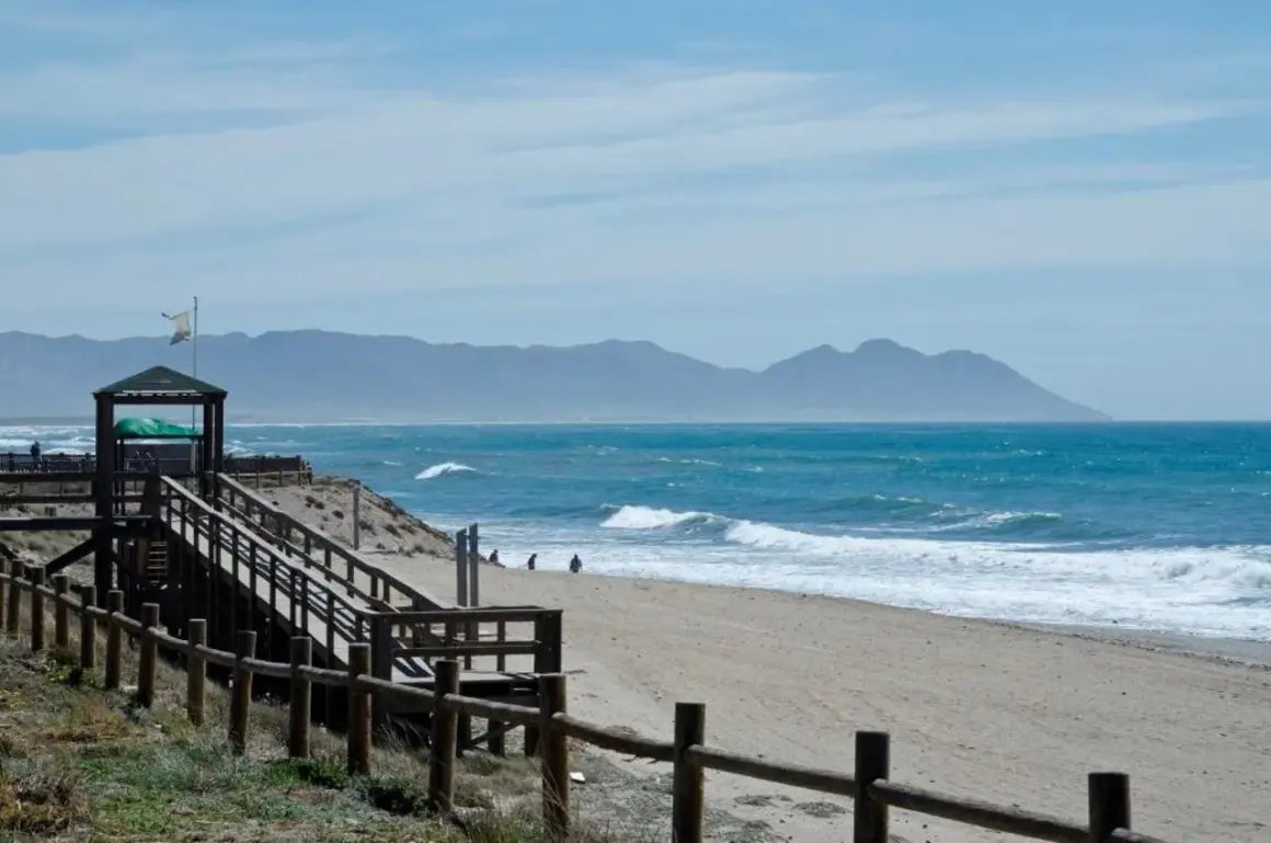 Un día perfecto para un paseo marítimo en Retamar. La arena dorada, el mar azul y las montañas de fondo crean un paisaje idílico.