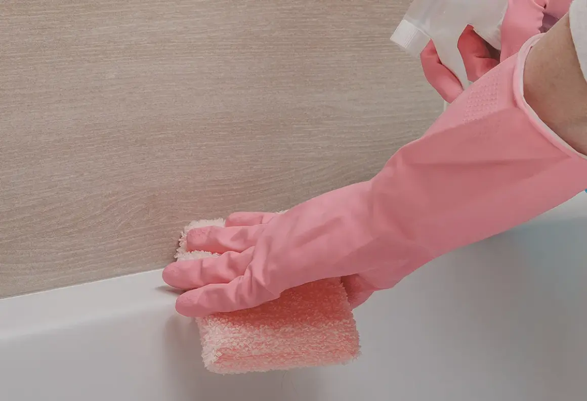 Main rose, une éponge rose nettoie le joint silicone jauni de la baignoire.