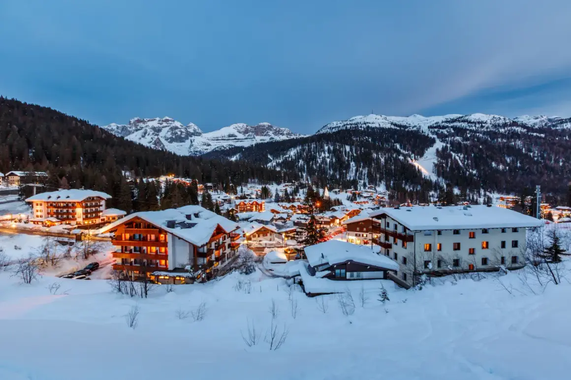 Paesaggio innevato di Madonna di Campiglio al crepuscolo. Hotel illuminati e montagne sullo sfondo, un invito a scoprire cosa vedere.