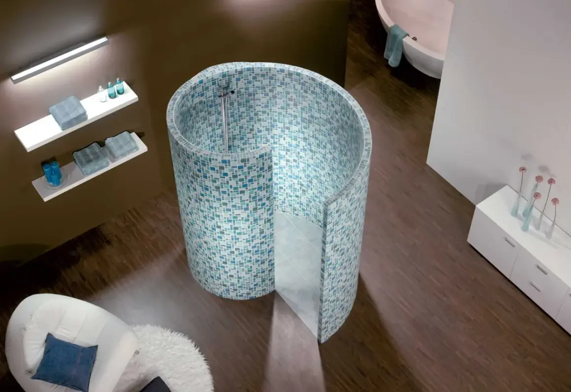 Une douche escargot aux mosaïques bleues et vertes, avec une baignoire et un fauteuil blanc dans une salle de bain moderne.
