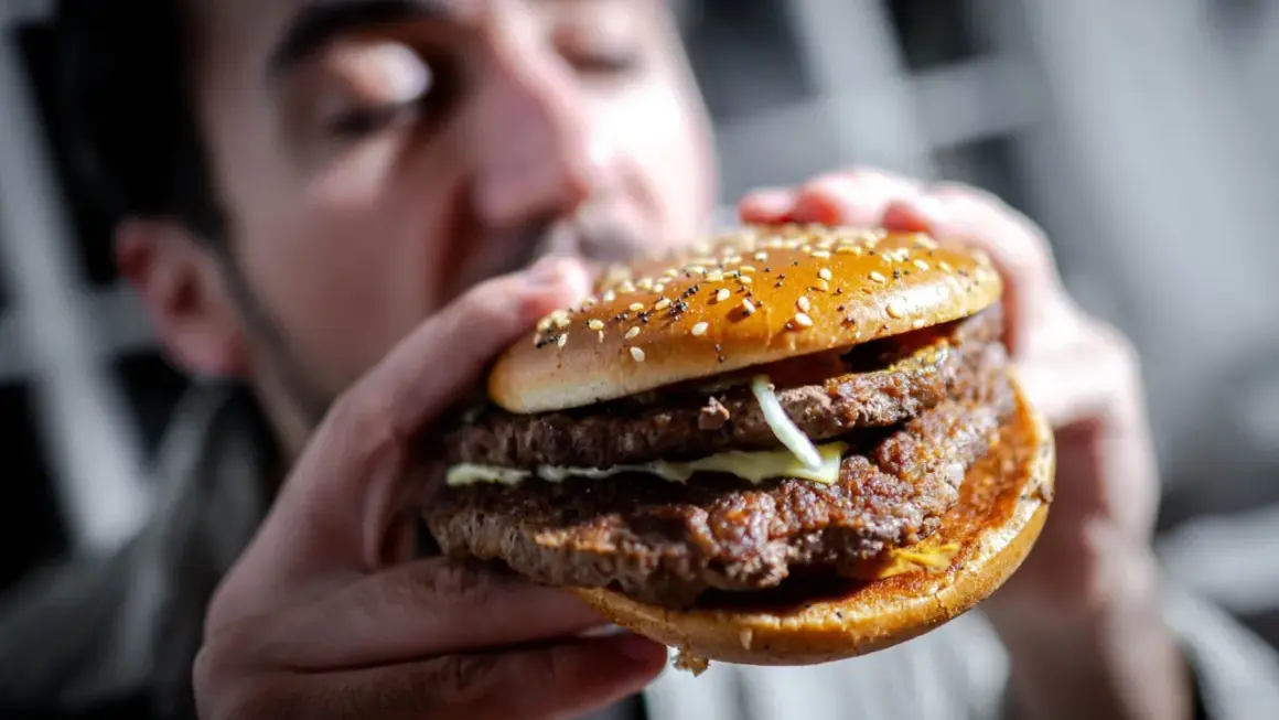 Mann hält einen saftigen Doppel-Cheeseburger mit Sesambrötchen. Perfekt für Burger Rezept Ideen!
