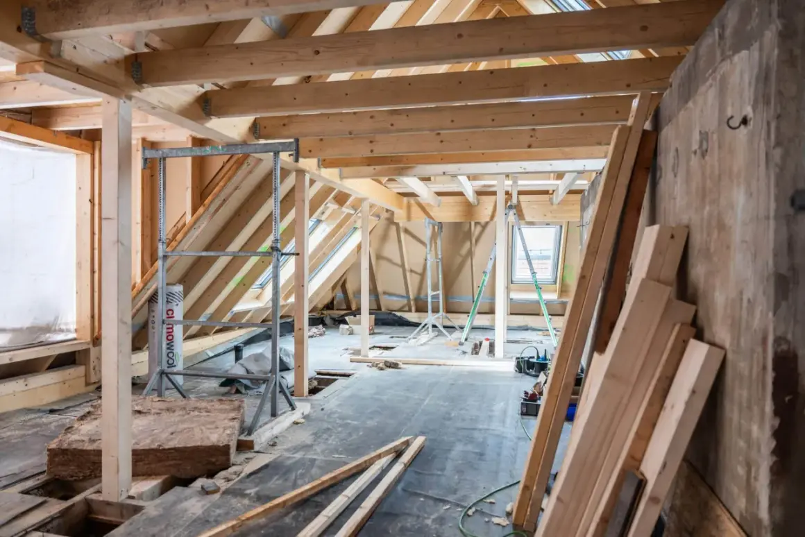 Chantier d'isolation des combles : charpente en bois, rouleaux d'isolant, échafaudages et matériaux de construction.