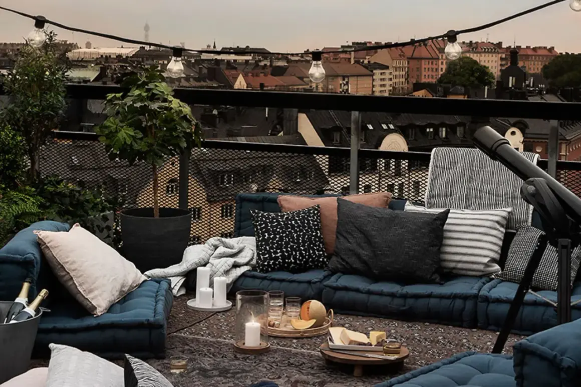 Gemütliches **outdoor wohnzimmer** auf einer Dachterrasse mit Blick auf die Stadt. Blaue Bodenkissen, Decken, Kerzen und eine Lichterkette schaffen Atmosphäre.