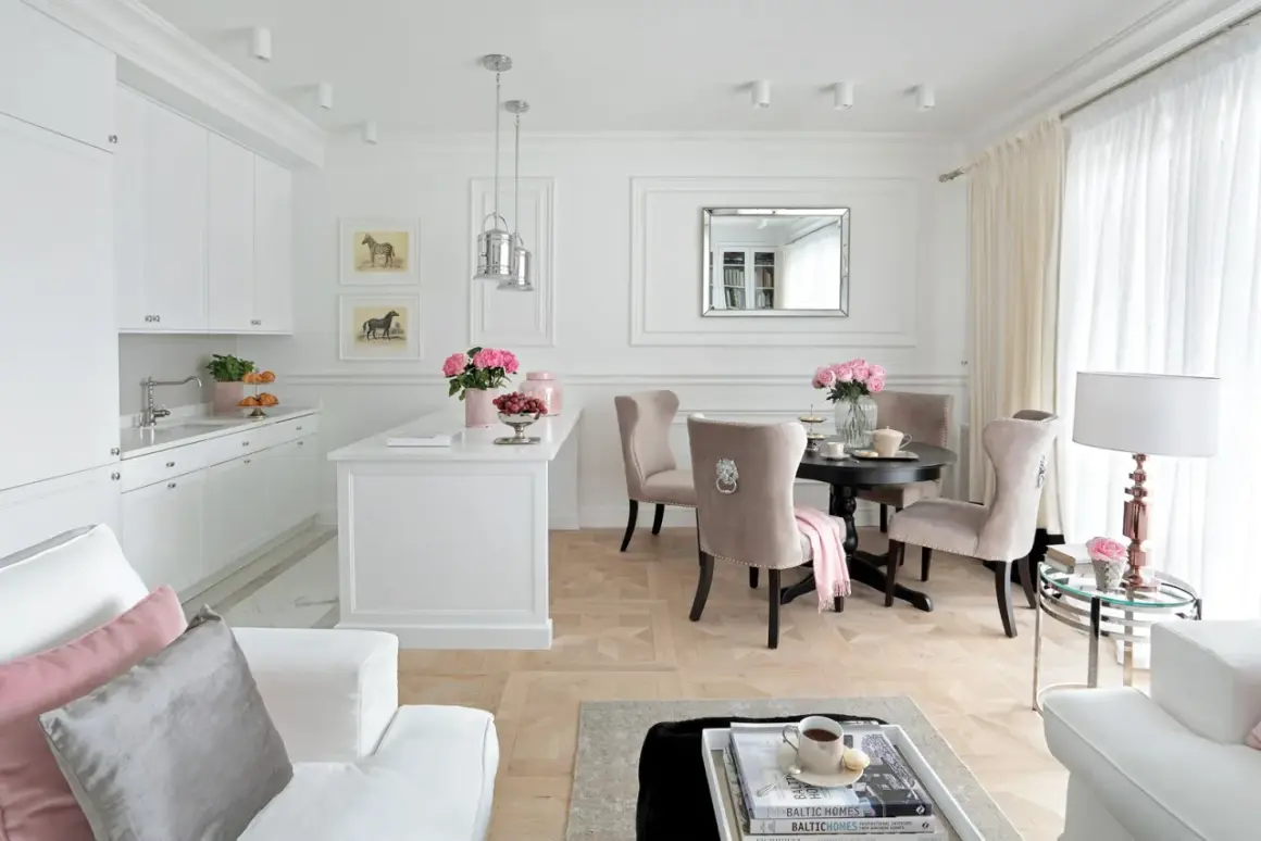 Elegancki salon z kuchnią inspiracje: białe meble, beżowe krzesła, okrągły stół, lustro, obrazy z końmi, kwiaty.