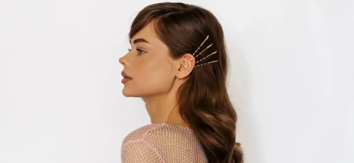 Frau mit welligen Haaren, die mit goldenen Haarnadeln und einem funkelnden Ohrstecker geschmückt sind.