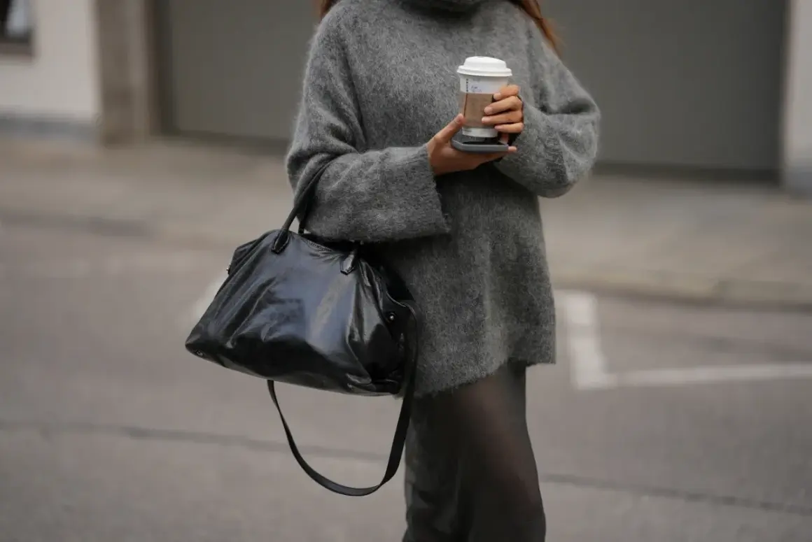Miękki, szary sweter damski dla puszystych, idealny na chłodne dni. Wygodny i stylowy, z dużą czarną torbą i kubkiem kawy.