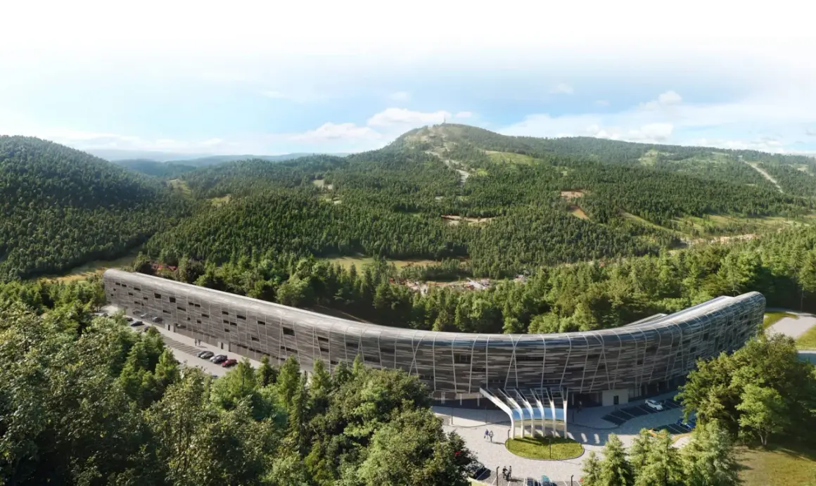 Nowoczesny, zakrzywiony budynek hotelu Mercure Szczyrk Resort otoczony lasem i górami.