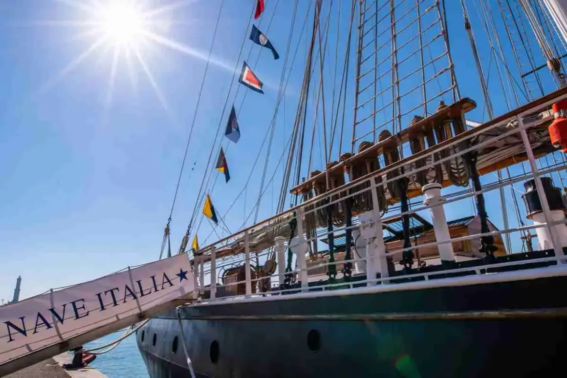 La nave Italia, con le sue vele spiegate e le bandiere colorate, si staglia contro il cielo azzurro.