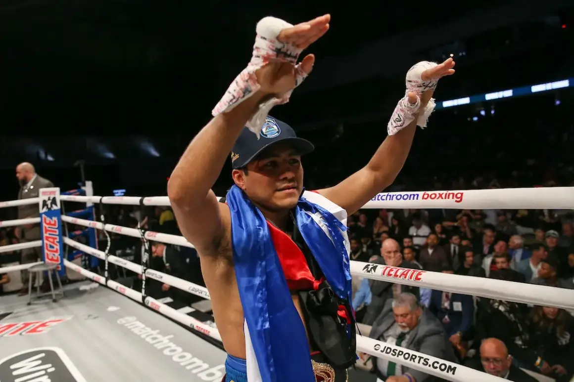 A victorious boxer, representing Nicaraguan pride, raises his taped hands in triumph in a packed arena.