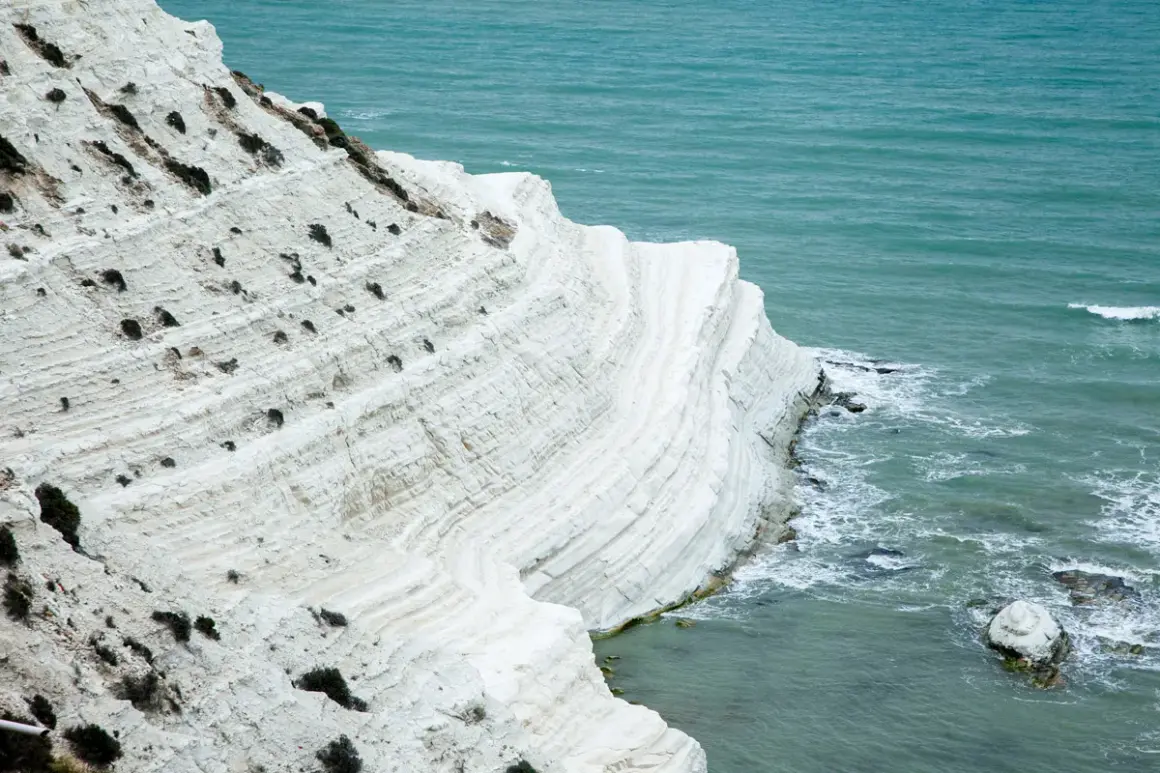 La scogliera bianca di Sicilia, con le sue stratificazioni calcaree, si tuffa nel mare turchese.
