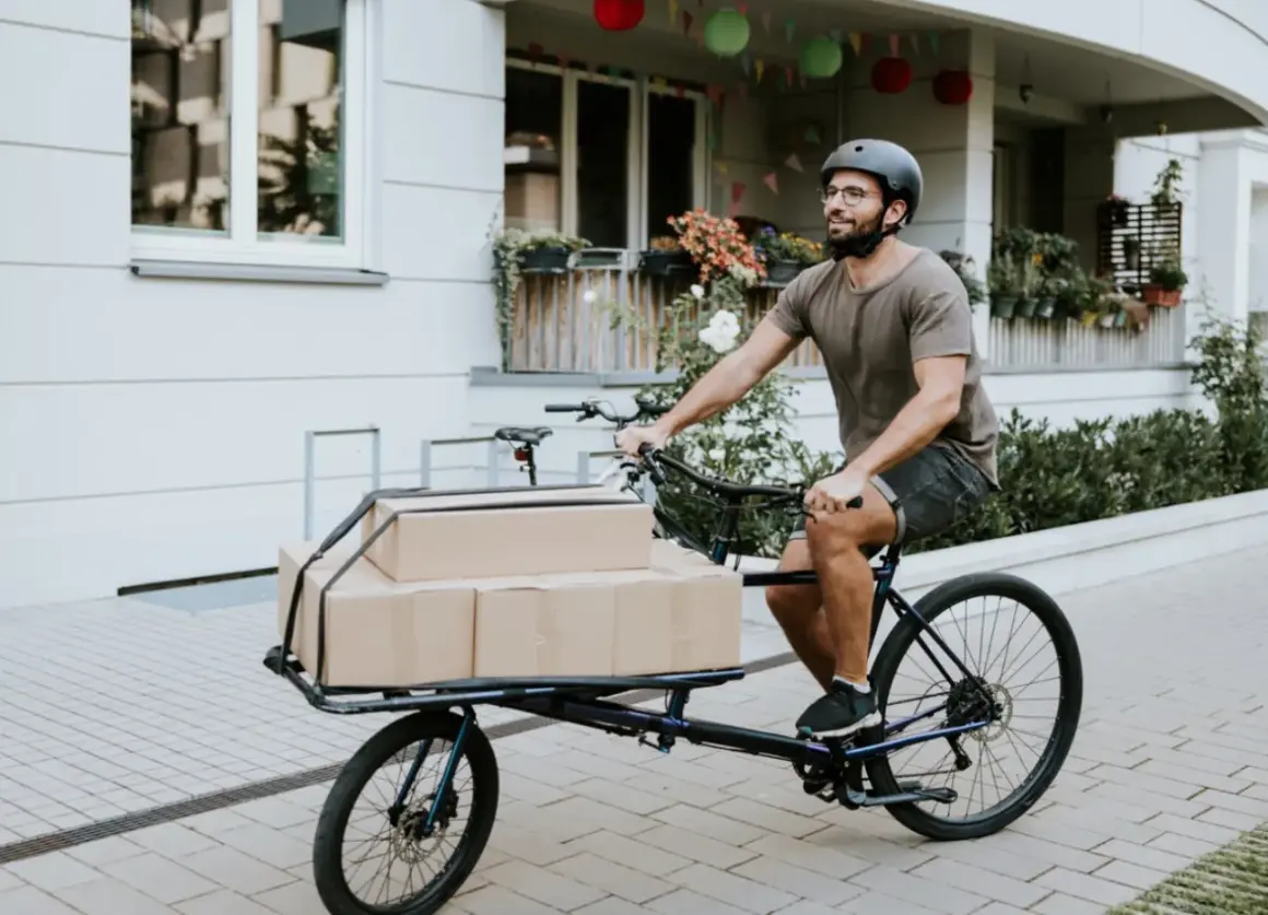Mann liefert Pakete mit einem Lastenrad. Eine gute Lastenrad Versicherung schützt vor unerwarteten Schäden.