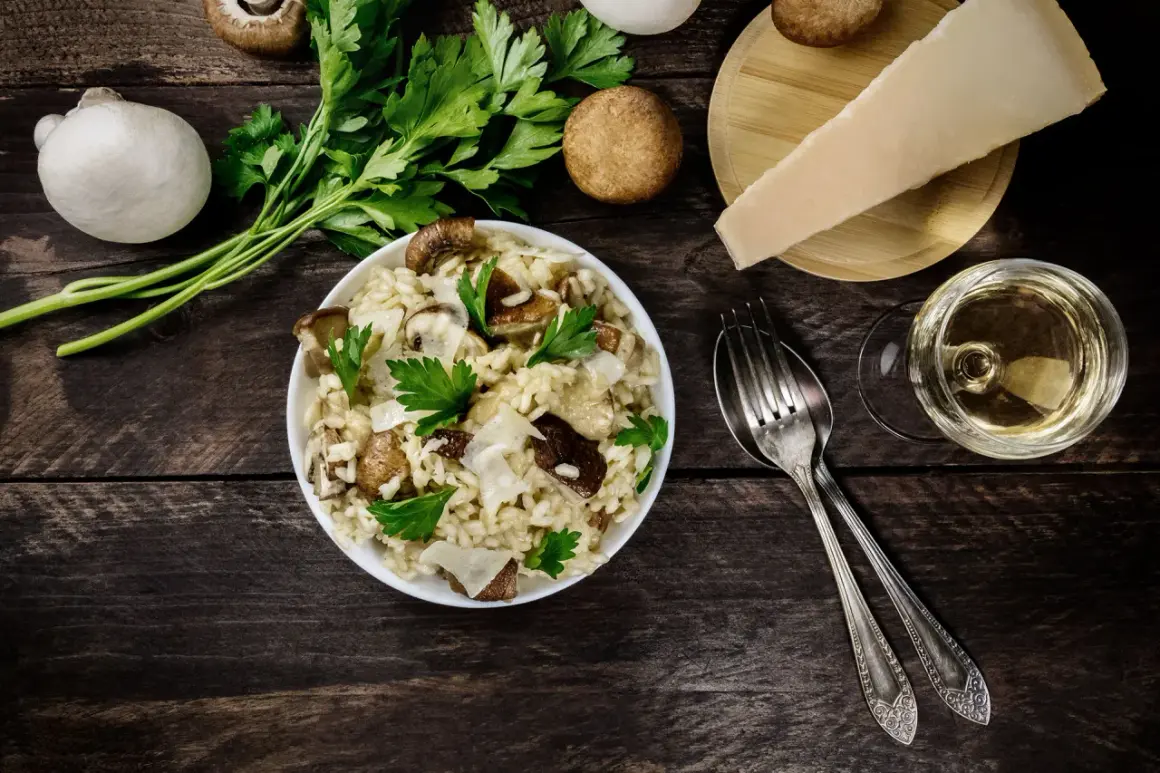 Risotto ai funghi cremoso, guarnito con prezzemolo fresco e scaglie di parmigiano. Un bicchiere di vino bianco completa questo perfetto abbinamento vino funghi.