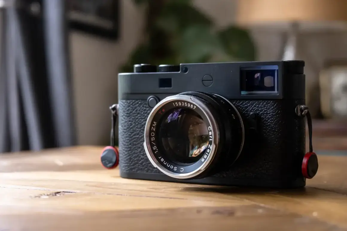 A black Leica M10P camera with a Carl Zeiss Sonnar lens sits on a wooden table, ready to capture life's moments.