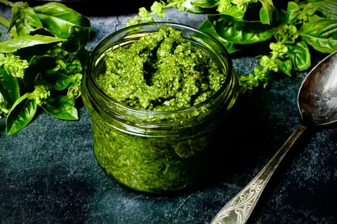 Frisches Basilikum-Pesto in einem Glas, bereit für ein köstliches basilikum pesto rezept. Daneben ein Löffel und grüne Basilikumblätter.