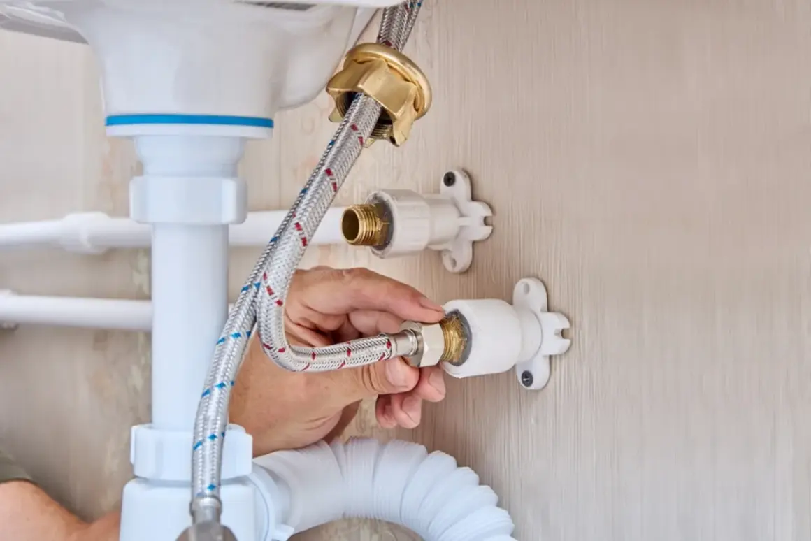 Mano conectando una manguera a la llave de paso de agua general, parte de la fontanería bajo un lavabo.