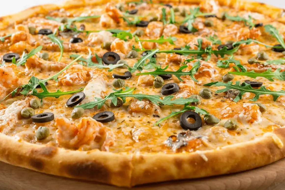 Pyszne ciasto na pizzę z krewetkami, oliwkami, kaparami i rukolą.