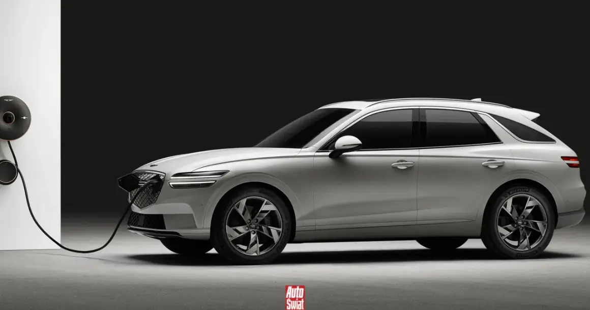 Biały Genesis GV70 na ładowarce. Elegancki SUV z charakterystycznym grillem i podwójnymi światłami.