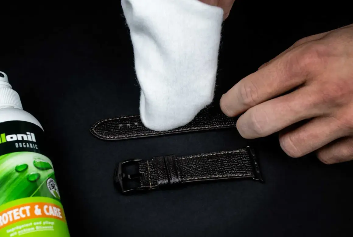 Ein weißes Tuch poliert ein dunkles Lederarmband. Daneben steht eine Flasche "Collonil Organic Protect & Care" zur Pflege.