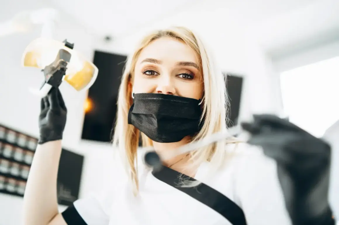 Uśmiechnięta dentystka w masce przygotowuje się do lakierowania zębów, trzymając lampę i narzędzia.