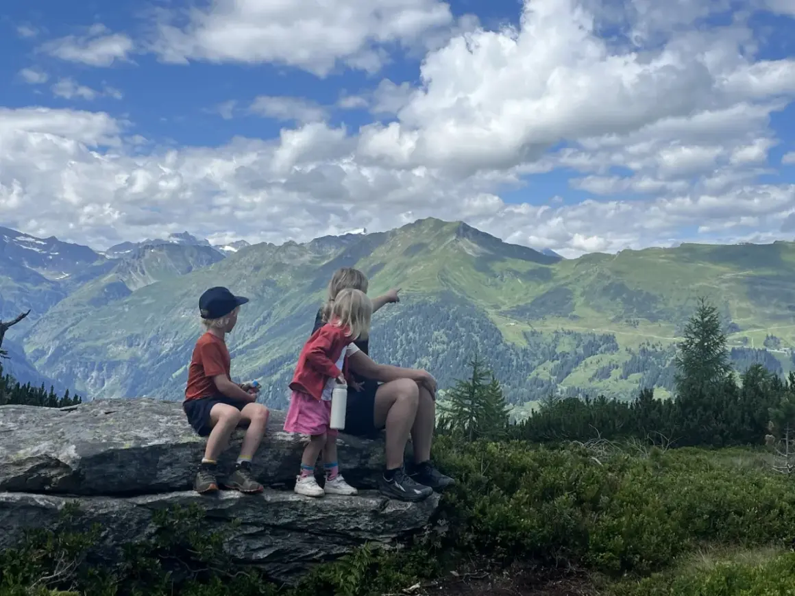 Familj njuter av en fantastisk utsikt under en bad gastein vandring. Barnen pekar ut över de gröna bergen och molnen.