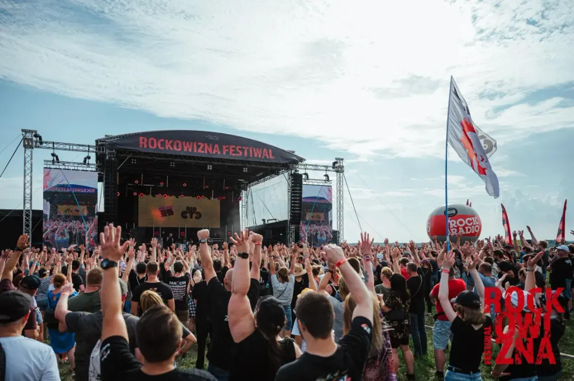 Tłum ludzi z rękami w górze na festiwalu Rockowizna przed sceną.