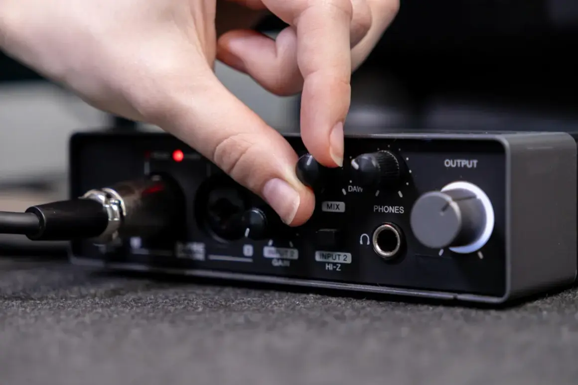 Dłoń kręci pokrętłem "MIX" na interfejsie audio, przygotowując się do podłączenia telefonu do wzmacniacza.