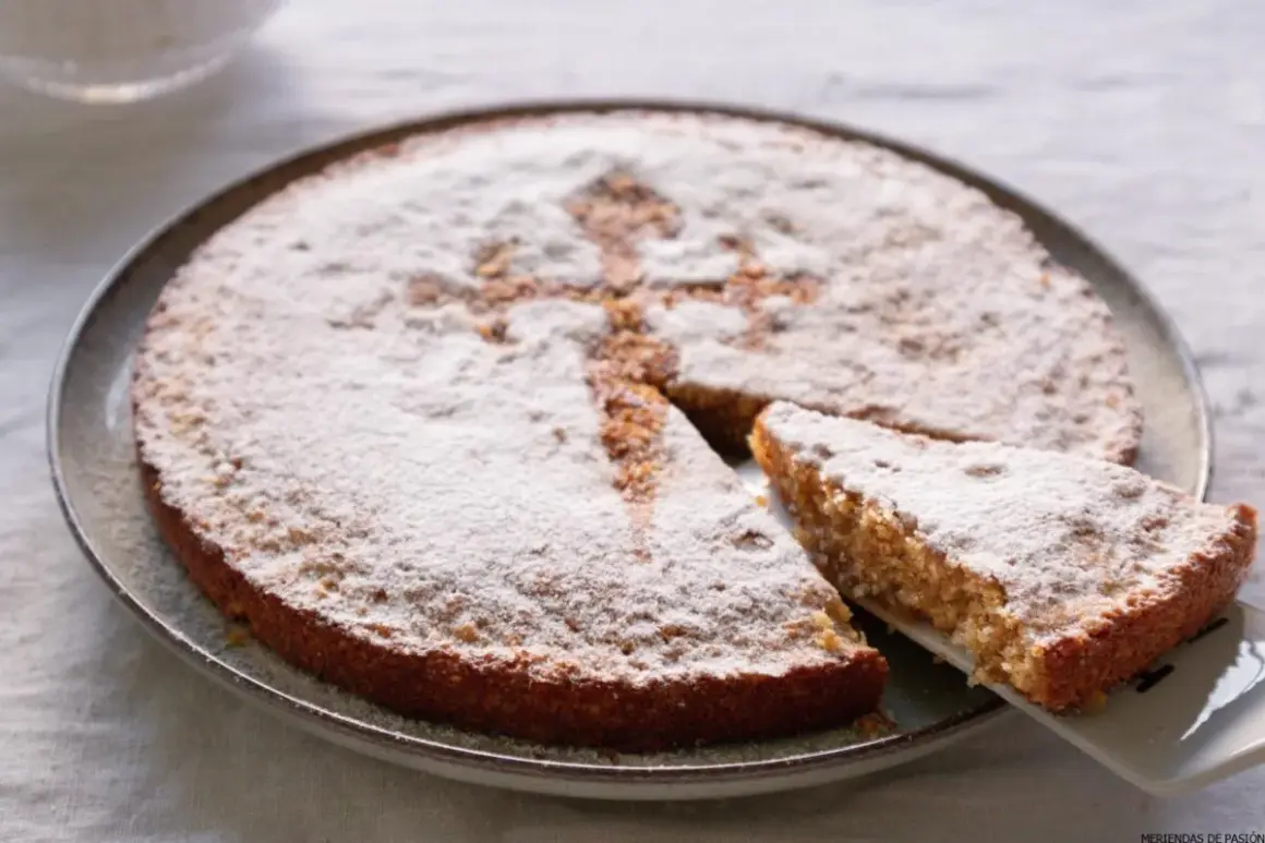 Tarta de Santiago, espolvoreada con azúcar glas, con una porción servida.