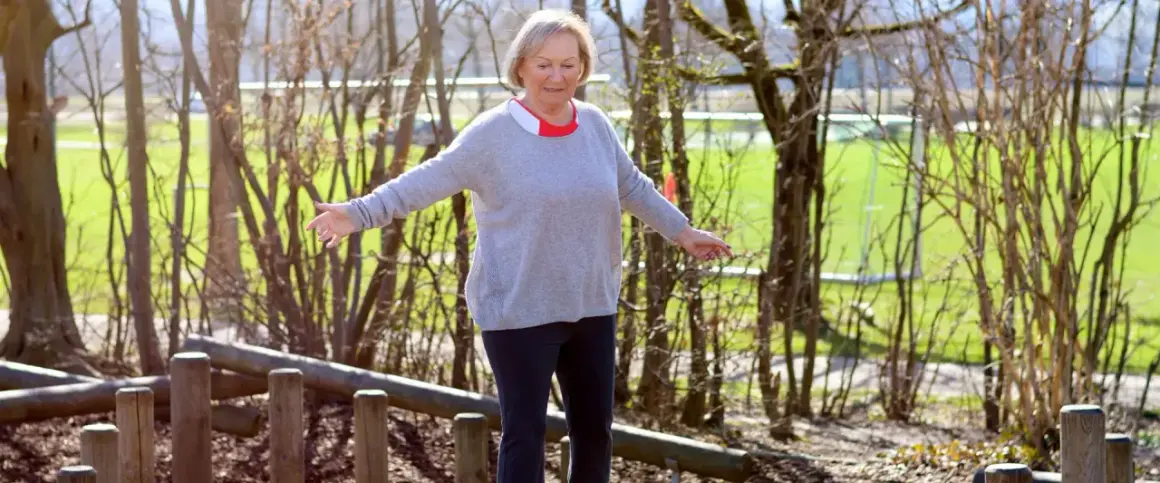 Ältere Frau balanciert auf Holzstämmen im Freien.