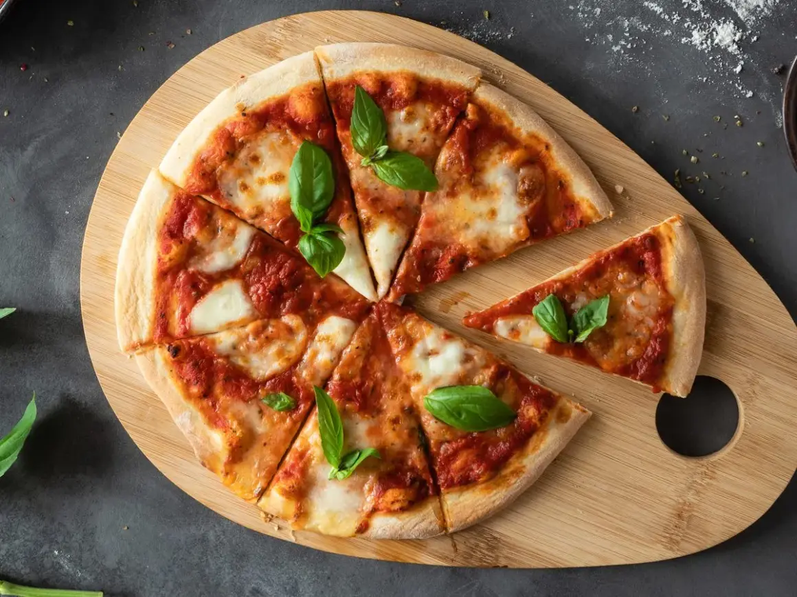 Ania gotuje ciasto na pizzę. Na drewnianej desce leży pyszna pizza margherita z bazylią, pokrojona na kawałki.
