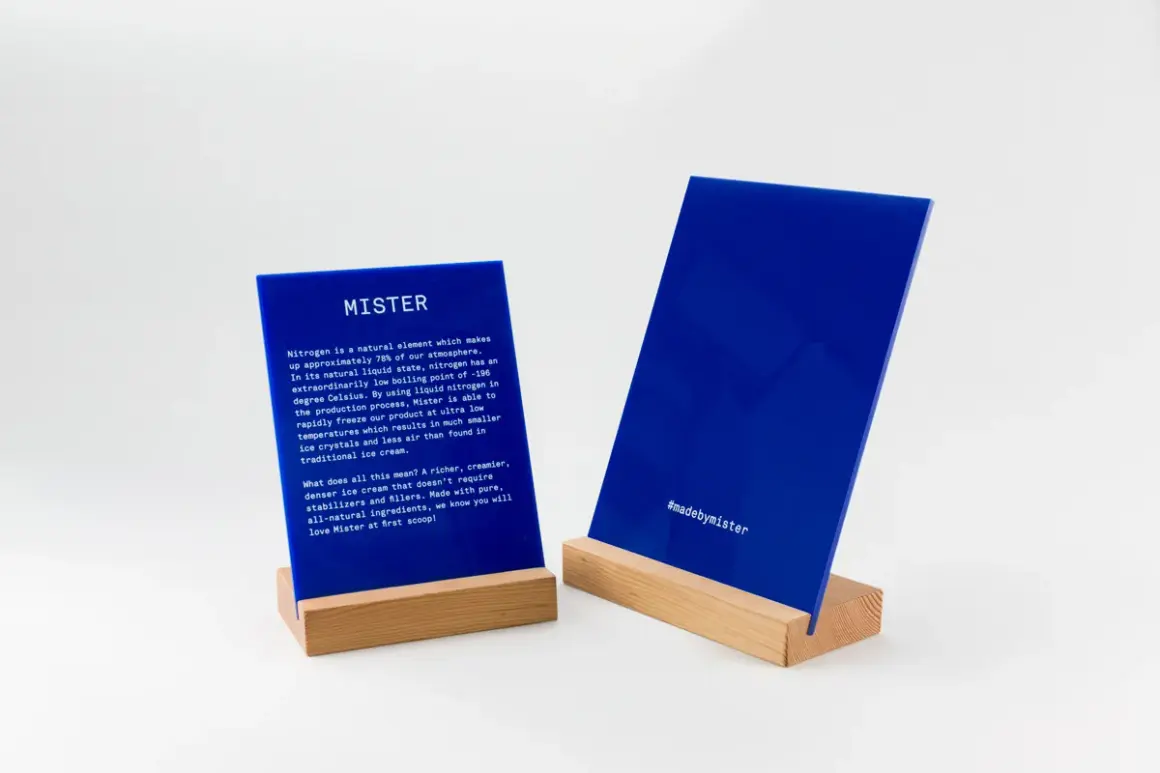 Deux panneaux en **lettre plexiglas** bleus sur des supports en bois. L'un décrit le processus de fabrication de Mister, l'autre affiche le hashtag #madebymister.