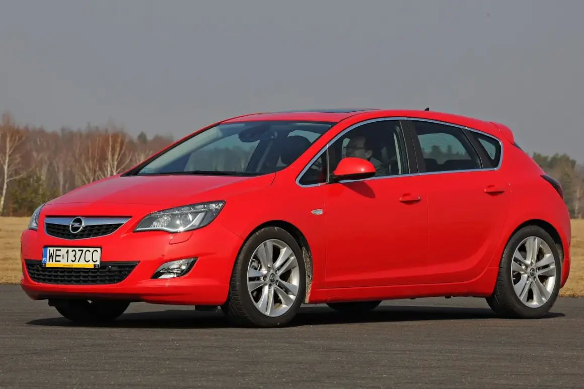 Czerwona Opel Astra na drodze. Kierowca za kierownicą. Jaki akumulator do tego modelu?