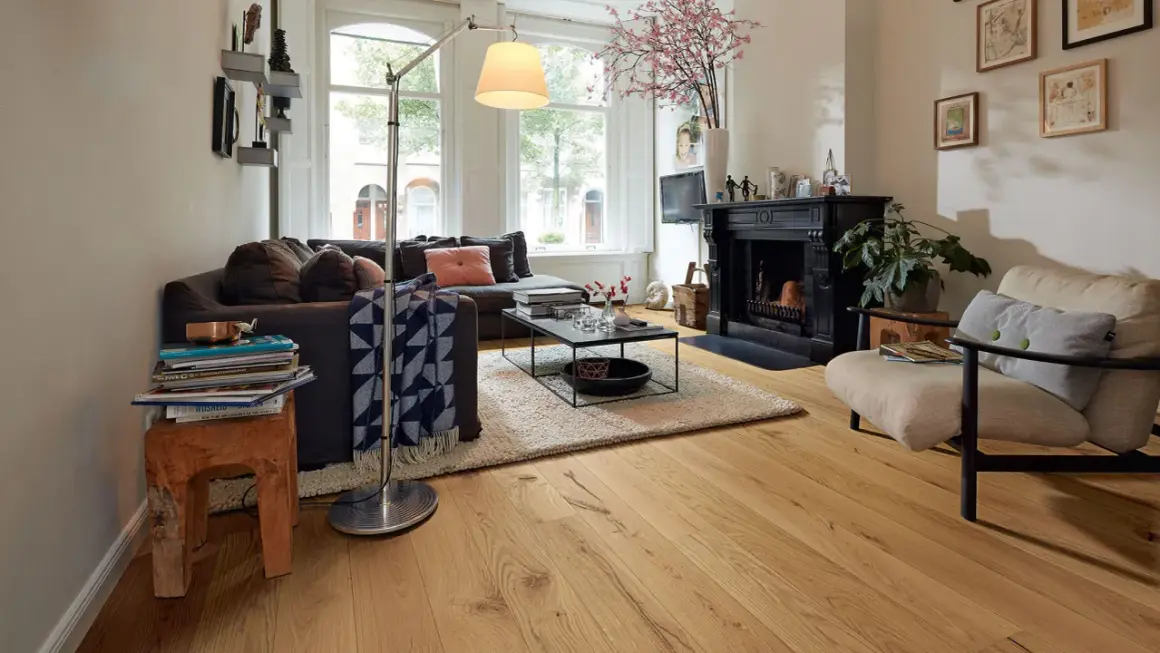 Gemütliches Wohnzimmer mit dunklem Sofa, Kamin und einem Sessel. Der used look des Holzboden und der Deko verleiht dem Raum Charakter.