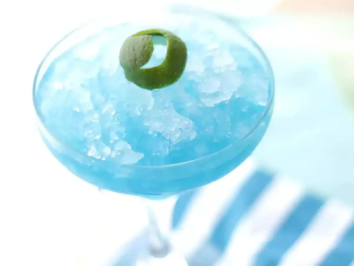 Orzeźwiający drink Błękitna Laguna, zmrożony i udekorowany skórką limonki, idealny na upalne dni.