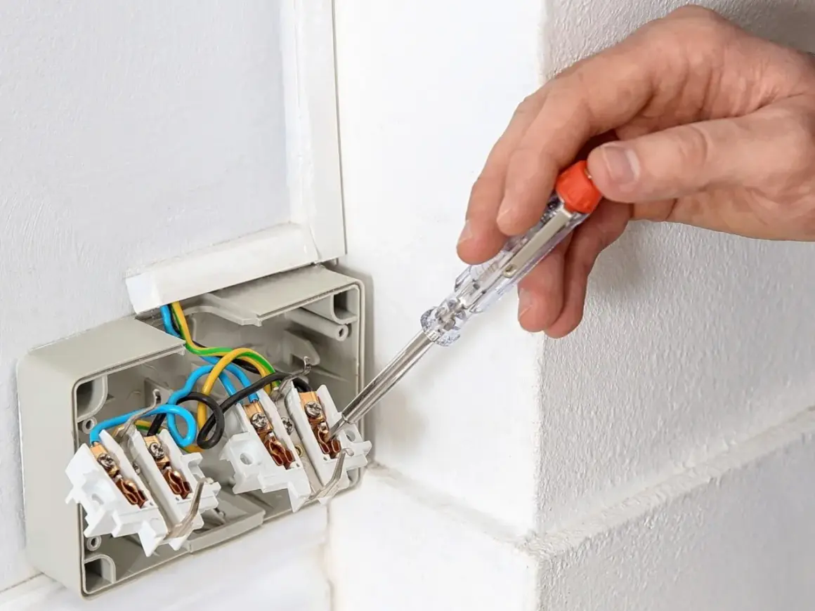 Ręka z próbnikiem napięcia sprawdza przewody w puszce elektrycznej. Dowiedz się, jak używać próbnik napięcia, by bezpiecznie pracować z instalacją.