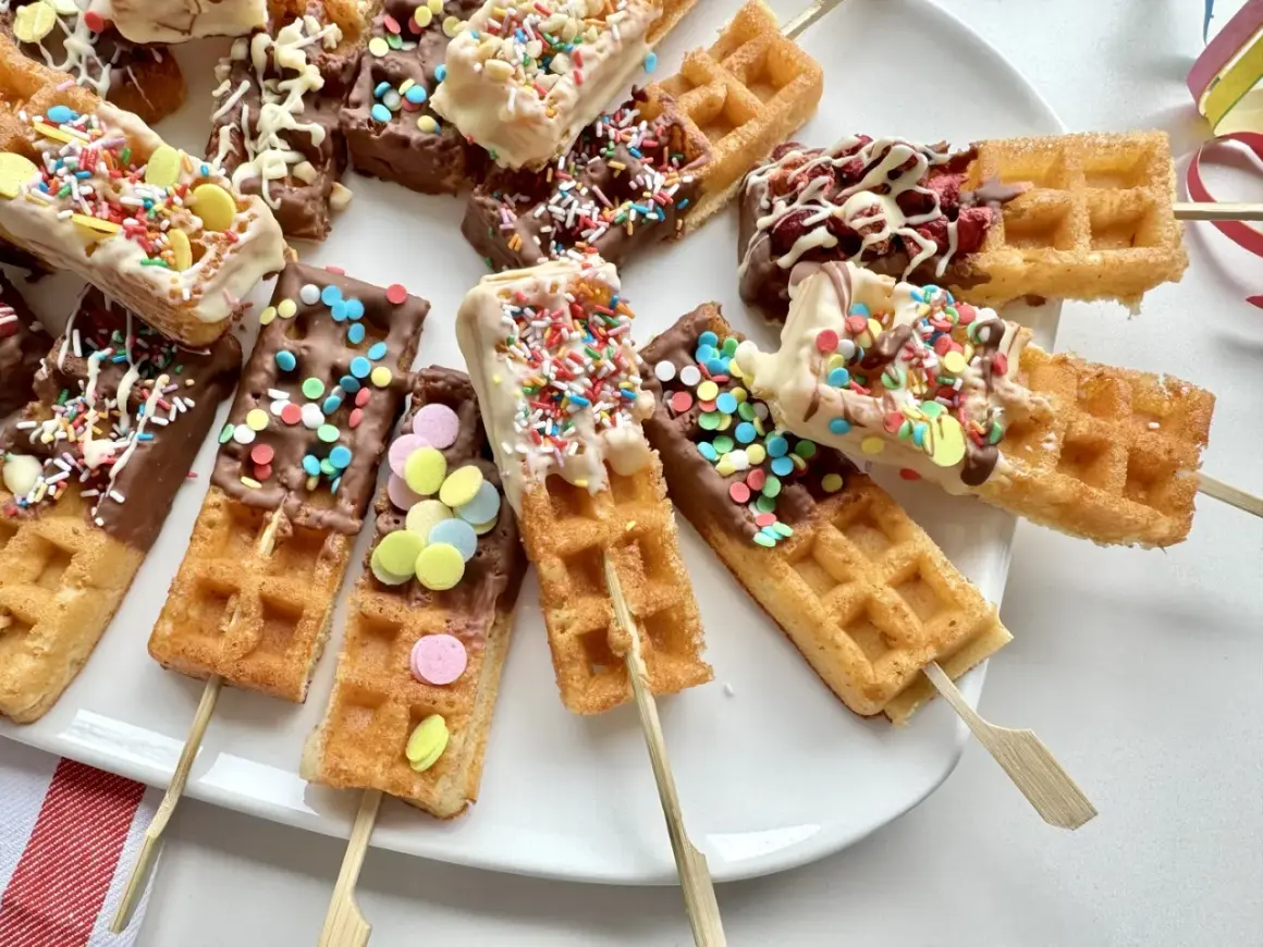 Bunte Waffeln am Stiel, getaucht in Schokolade und bestreut mit Streuseln und bunten Zuckerlinsen, laden zum Naschen ein.