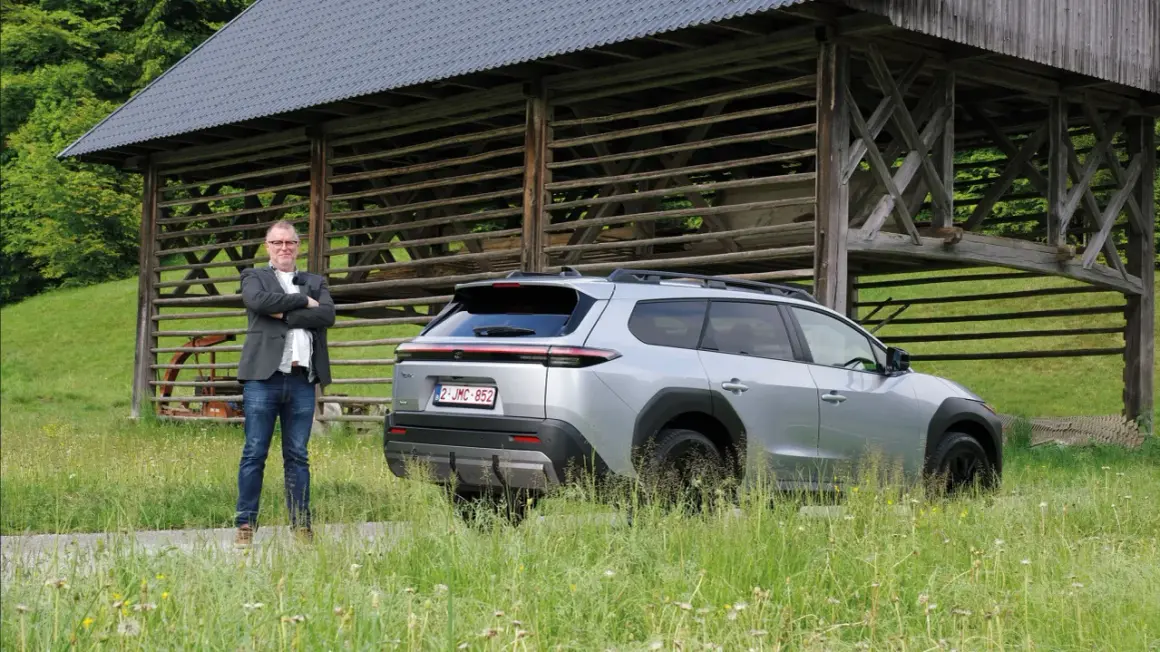 Man i kavaj står bredvid silverfärgad Toyota bz4x under ett gammalt träskjul.