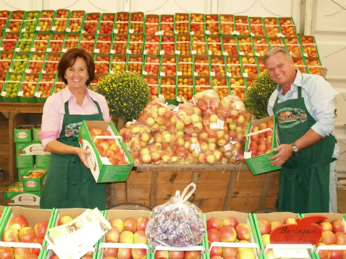 Ein Paar präsentiert Äpfel auf dem markt leichlingen. Sie halten Kisten mit frischen Äpfeln, umgeben von weiteren Obstkisten.