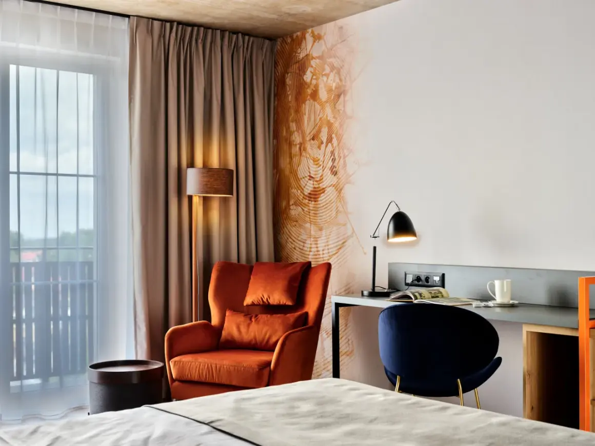 Przytulny pokój w **Bergo Hotel Szklarska Poręba**: pomarańczowy fotel, biurko z lampką i granatowe krzesło.