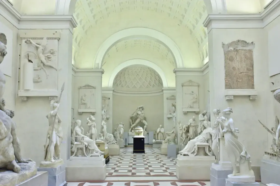 Interno della Galleria dell'Accademia con sculture classiche in marmo bianco, pavimentazione a scacchi e soffitto a volta.
