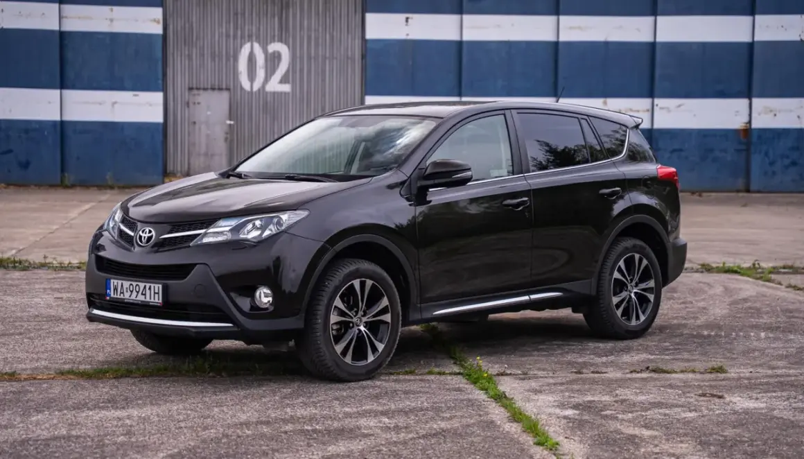 Czarny, używany Toyota RAV4 z salonu, zaparkowany przed budynkiem z numerem 02.
