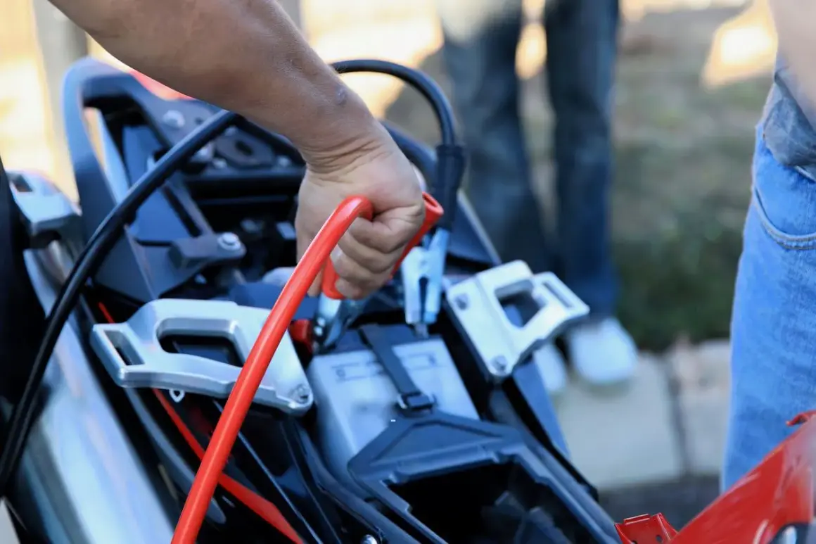 Mano sujetando pinza roja para desconectar batería moto.