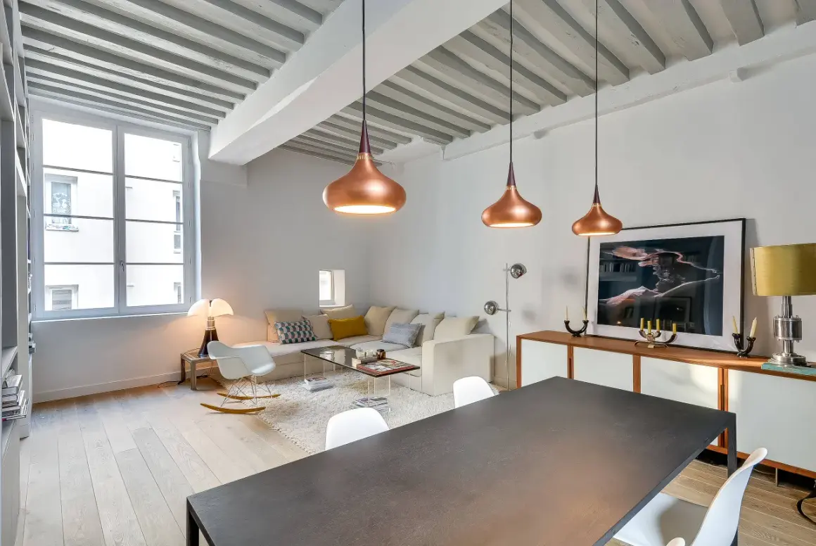 Lámparas colgantes de cobre y un diseño moderno reflejan las **últimas tendencias iluminación salones**. Un sofá blanco y una mesa de comedor completan el espacio.