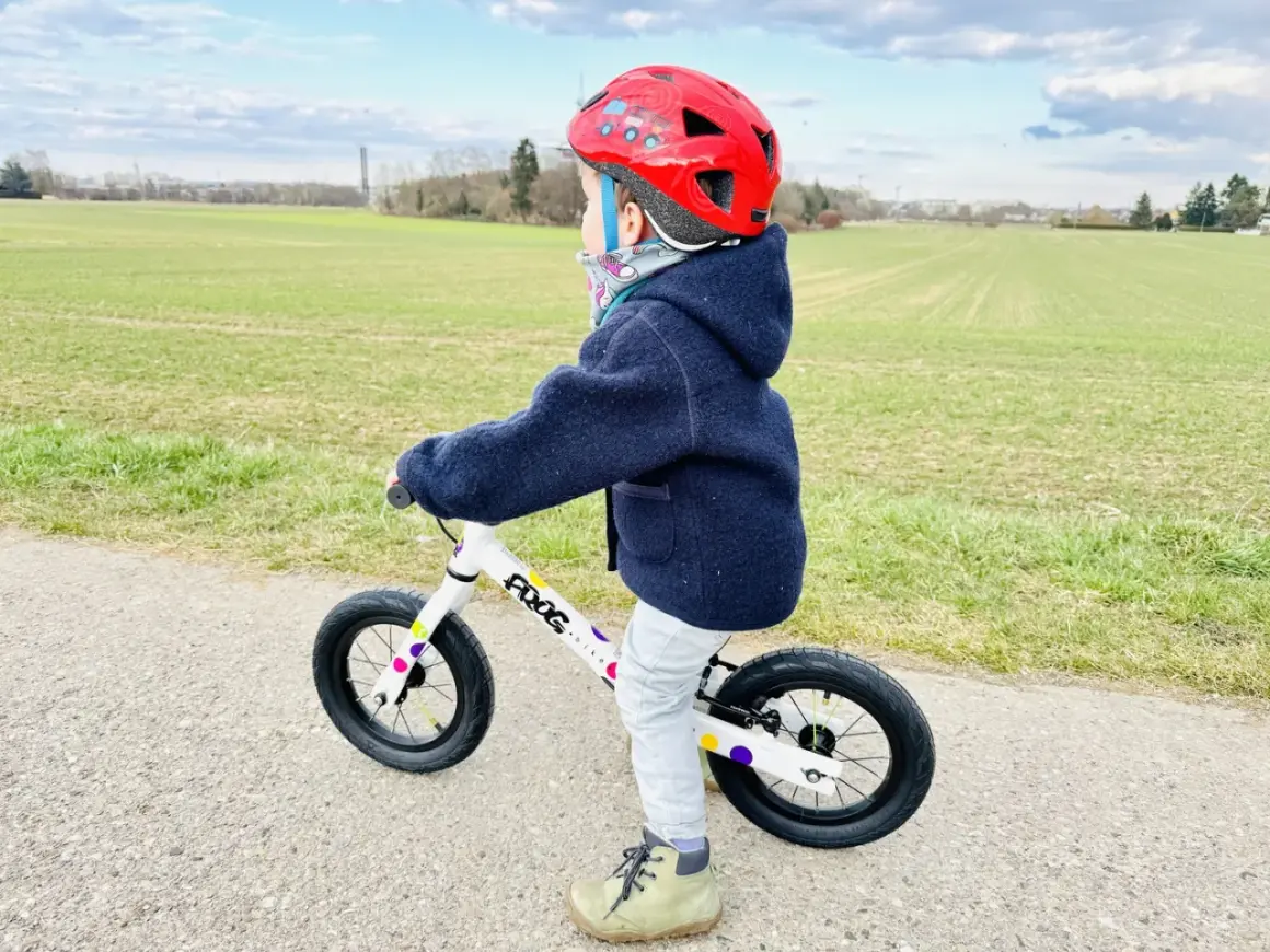Kind mit rotem Helm übt das laufrad fahren auf einem Feldweg.