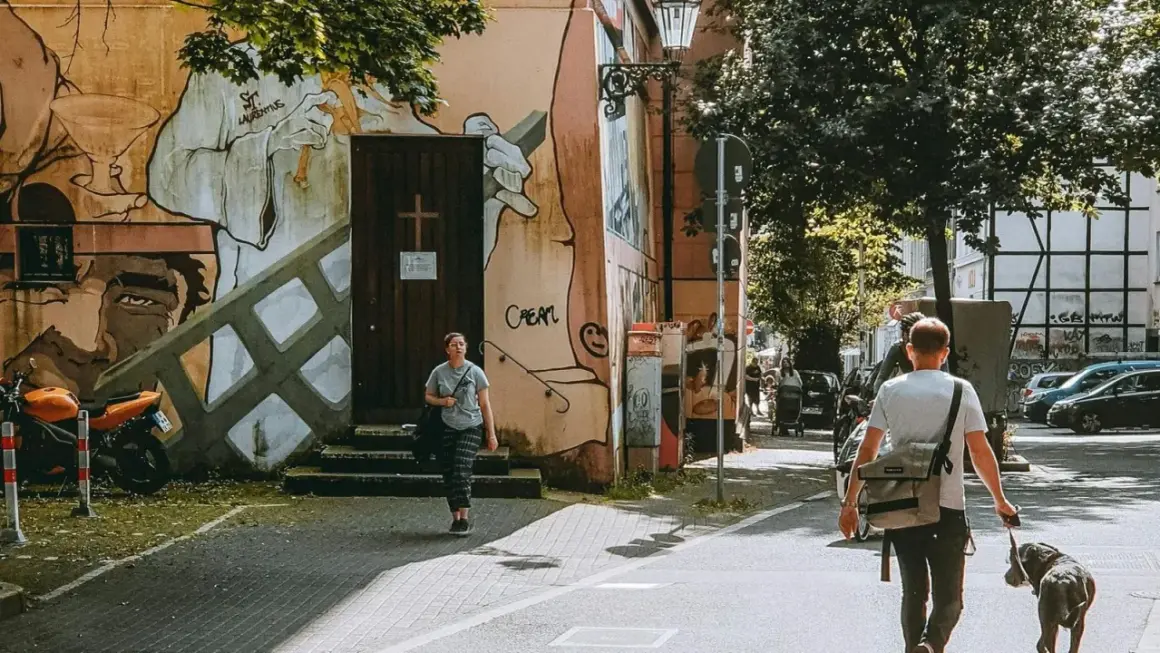 Ein Mann geht mit Hund durch eine Straße in Wuppertal, vorbei an einer Wand mit Graffiti.