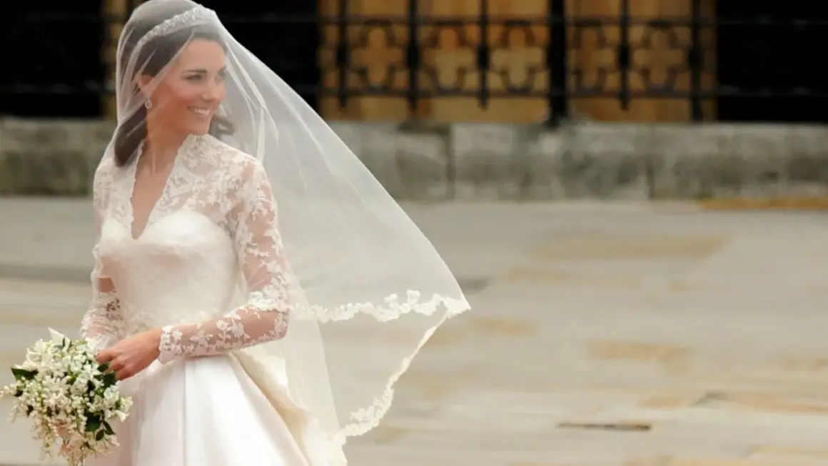 Kate Middleton sposa, radiosa nel suo abito bianco con pizzo e velo, tiene un bouquet di fiori.