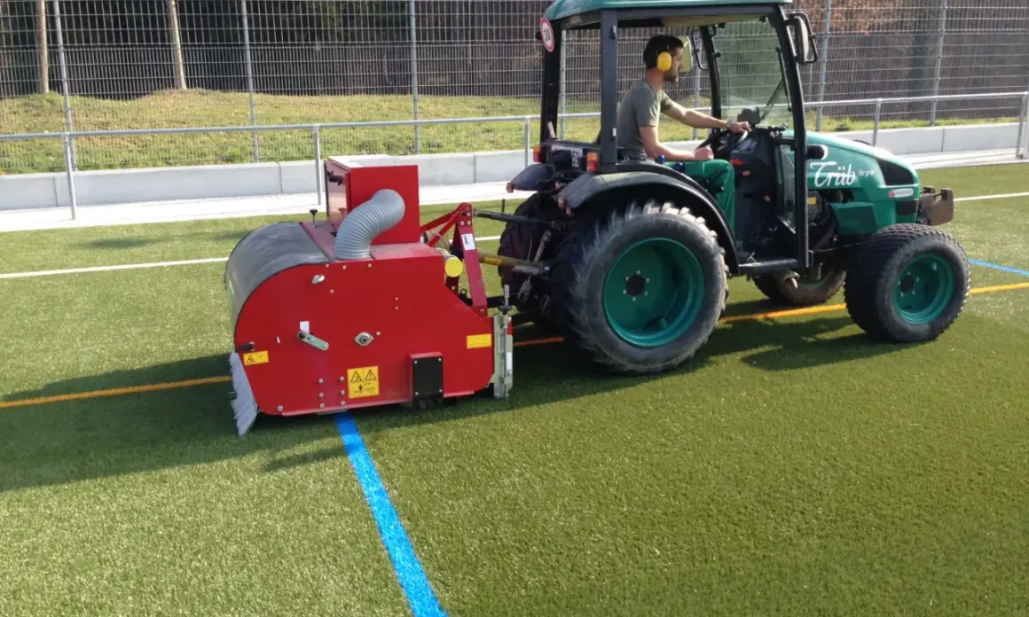 Traktor mit Anbaugerät reinigt Kunstrasen.