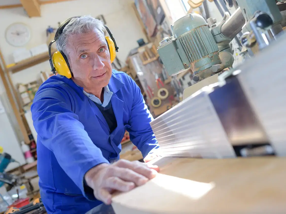 Ein Mann in Schutzkleidung arbeitet an einer Holzbearbeitungsmaschine. Seine Erfahrung im Handwerk spiegelt sich in seinen **altersteilzeit erfahrungsberichte** wider.