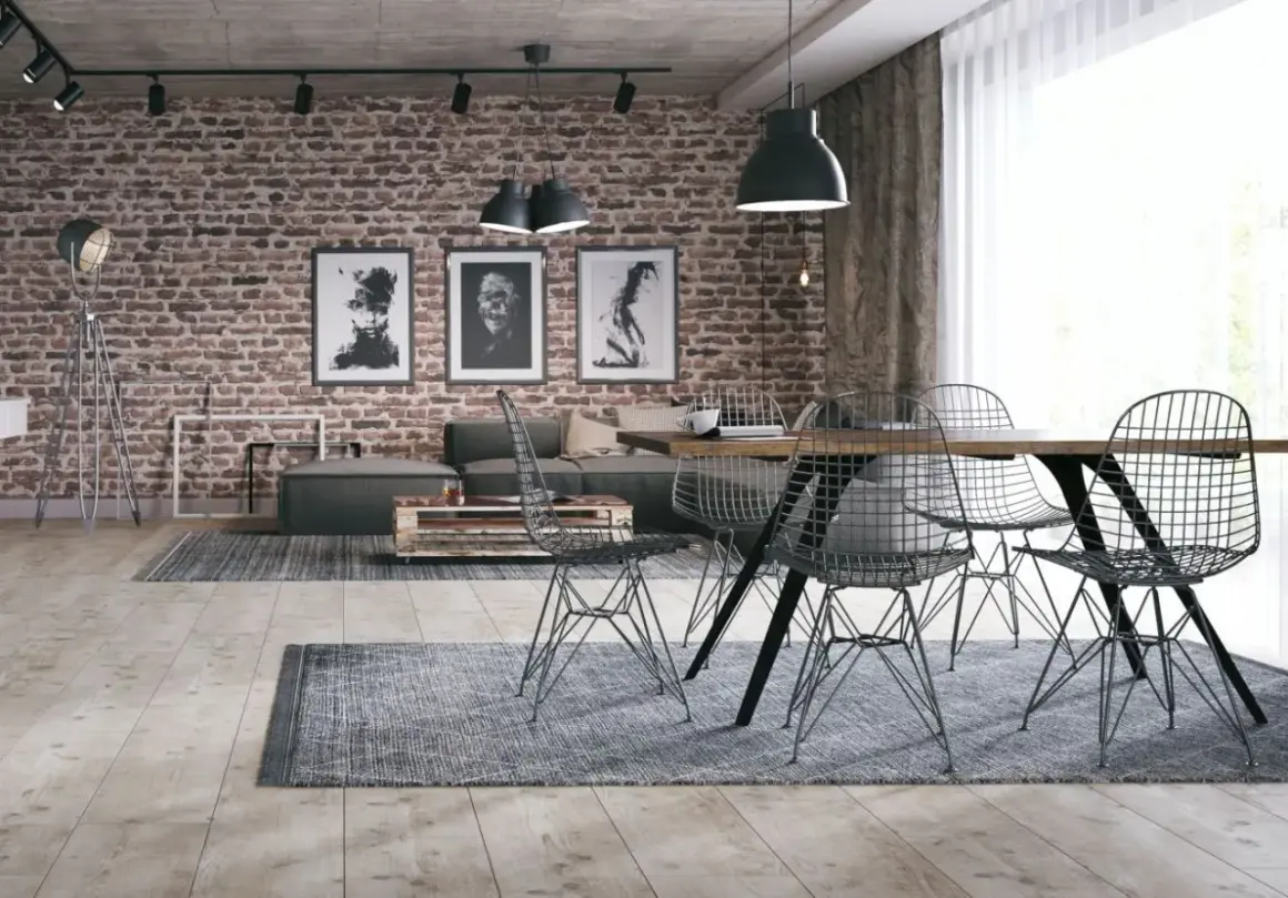 Surowy, betonowy sufit w stylu loft nadaje wnętrzu industrialnego charakteru. Ceglana ściana, grafiki i metalowe meble dopełniają ten surowy klimat.